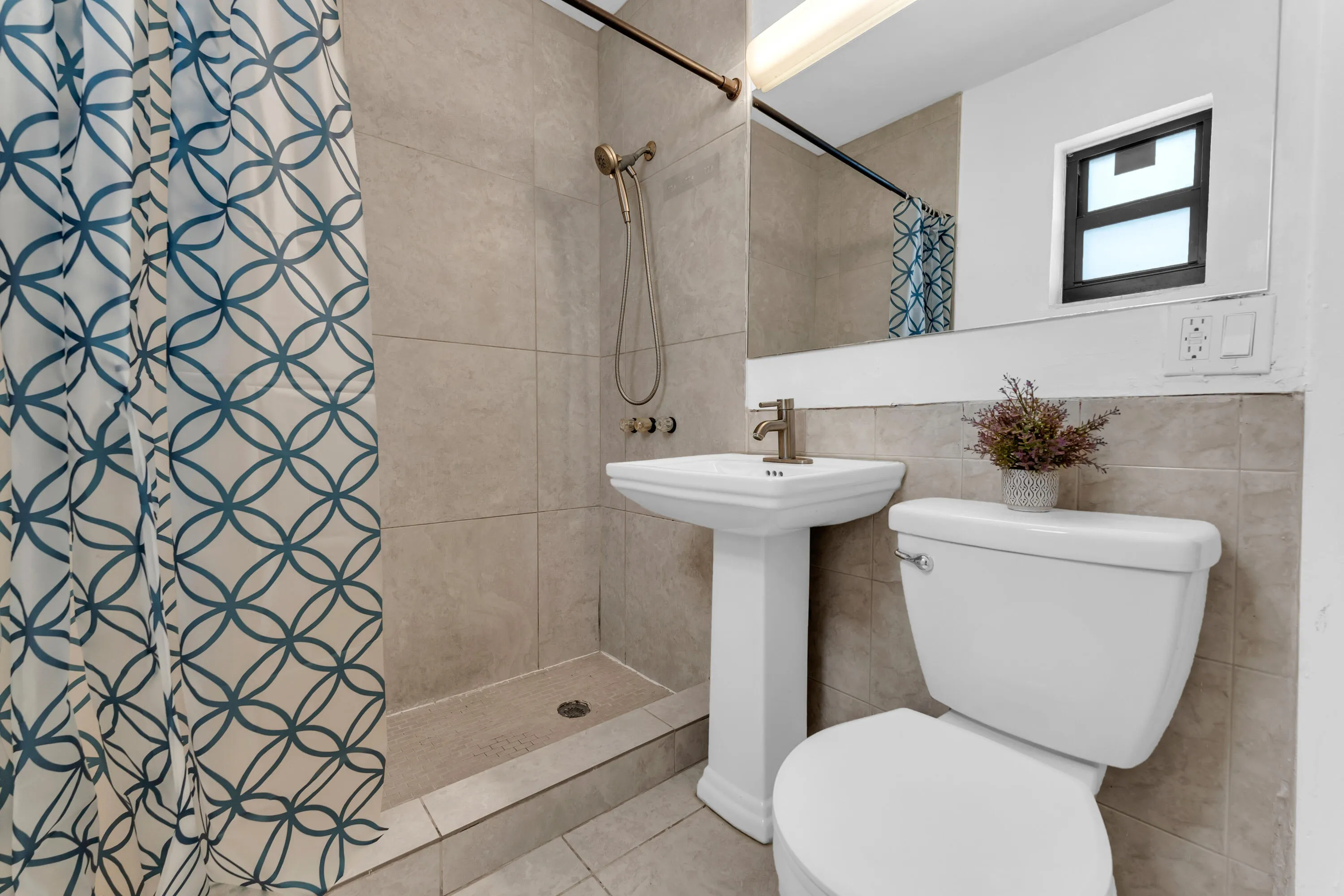 Pedestal sink with brushed nickel faucet, ceramic tiled walls, and a shower with a handheld fixture