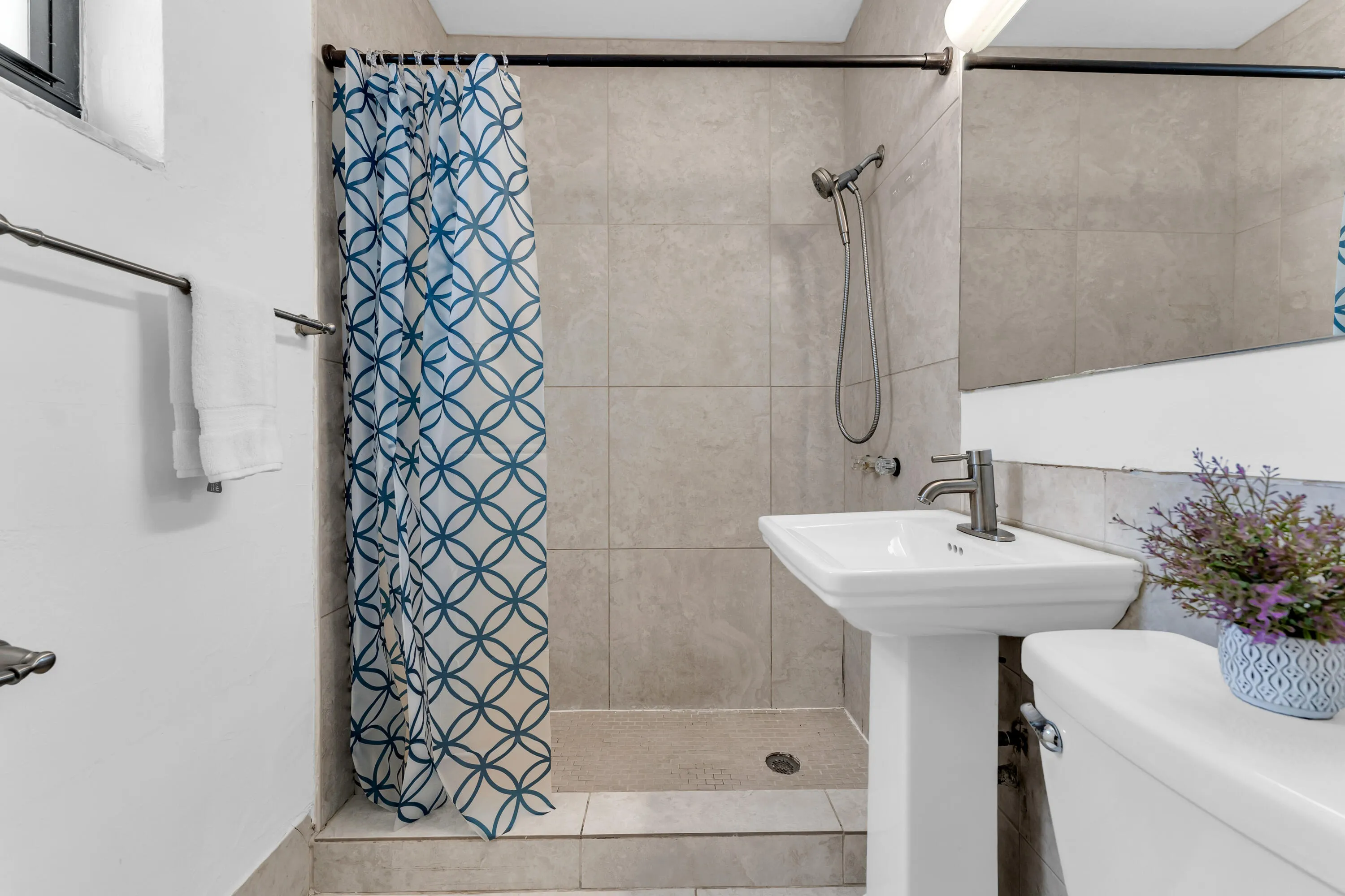 Contemporary bathroom featuring a pedestal sink, matte black faucet, and a tiled shower with a handheld showerhead