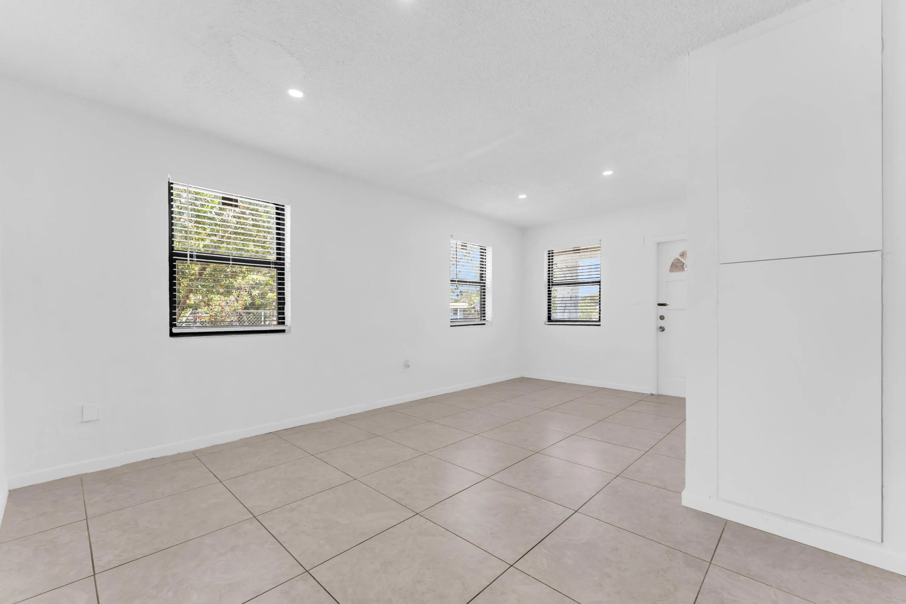 Spacious interior featuring neutral tile flooring, recessed lighting, multiple windows with blinds, and built-in cabinetry