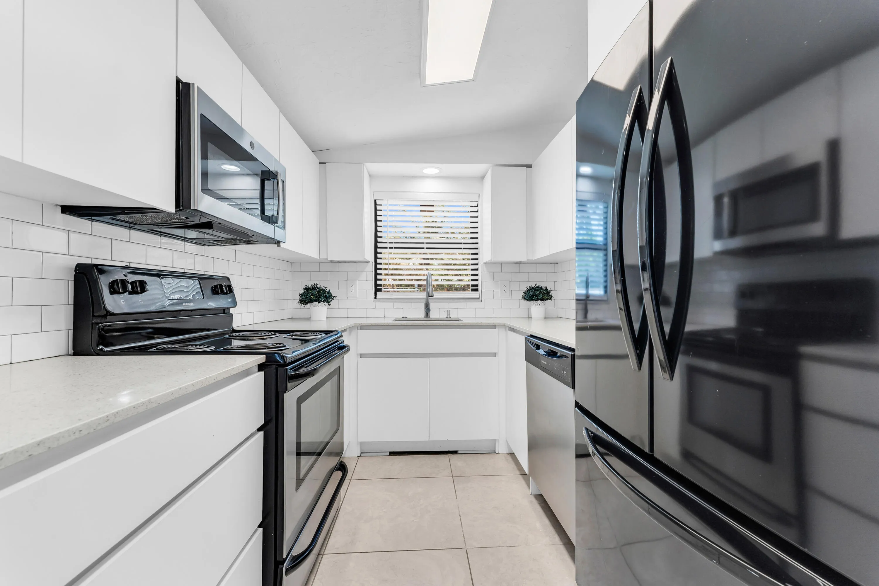 Modern kitchen featuring white cabinetry, light-toned countertops, subway tile backsplash, and stainless steel appliances including an over-the-range microwave and dishwasher