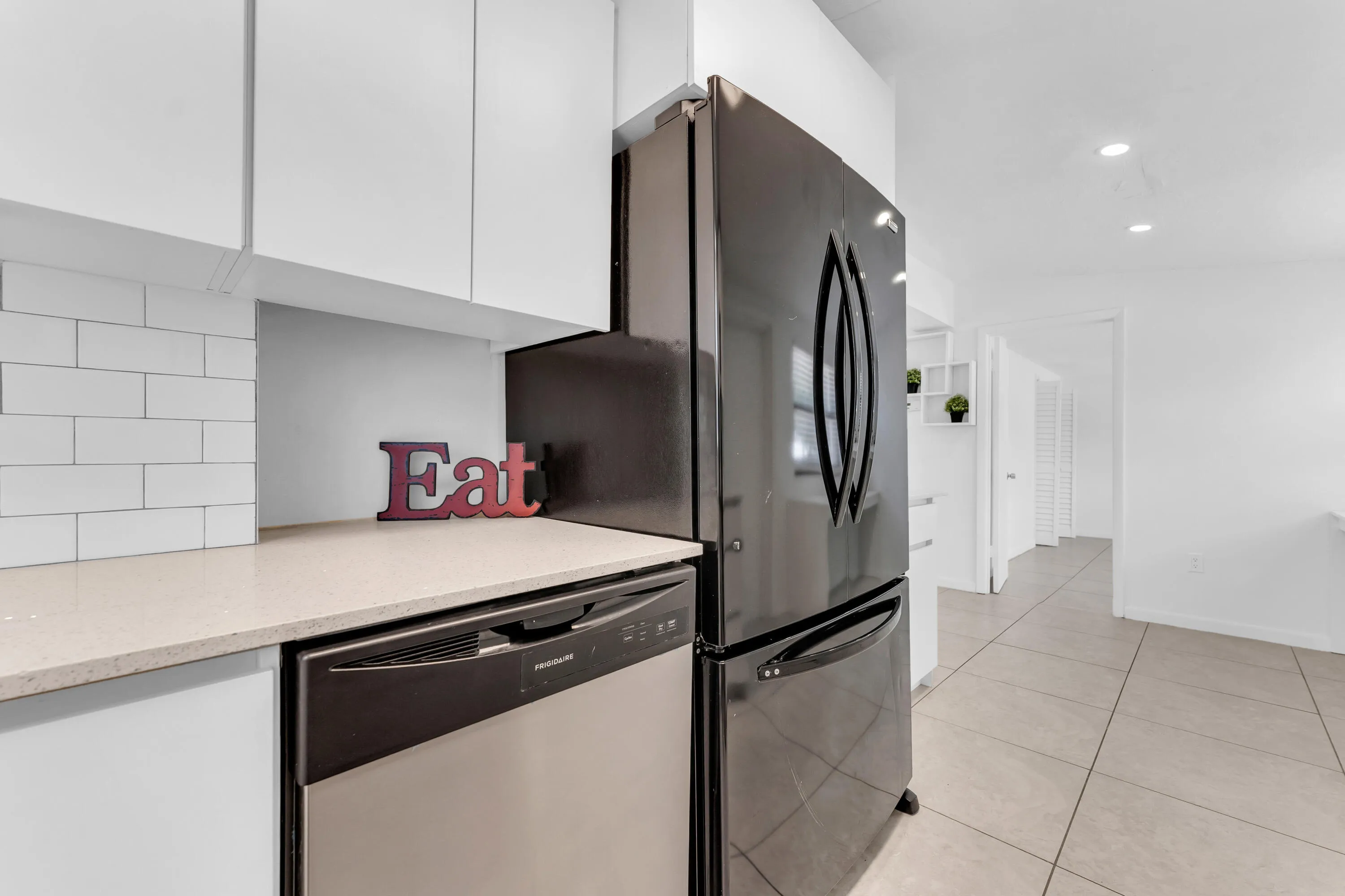 Modern kitchen featuring a stainless steel refrigerator, integrated dishwasher, light-toned countertop, white subway tile backsplash, and white cabinetry