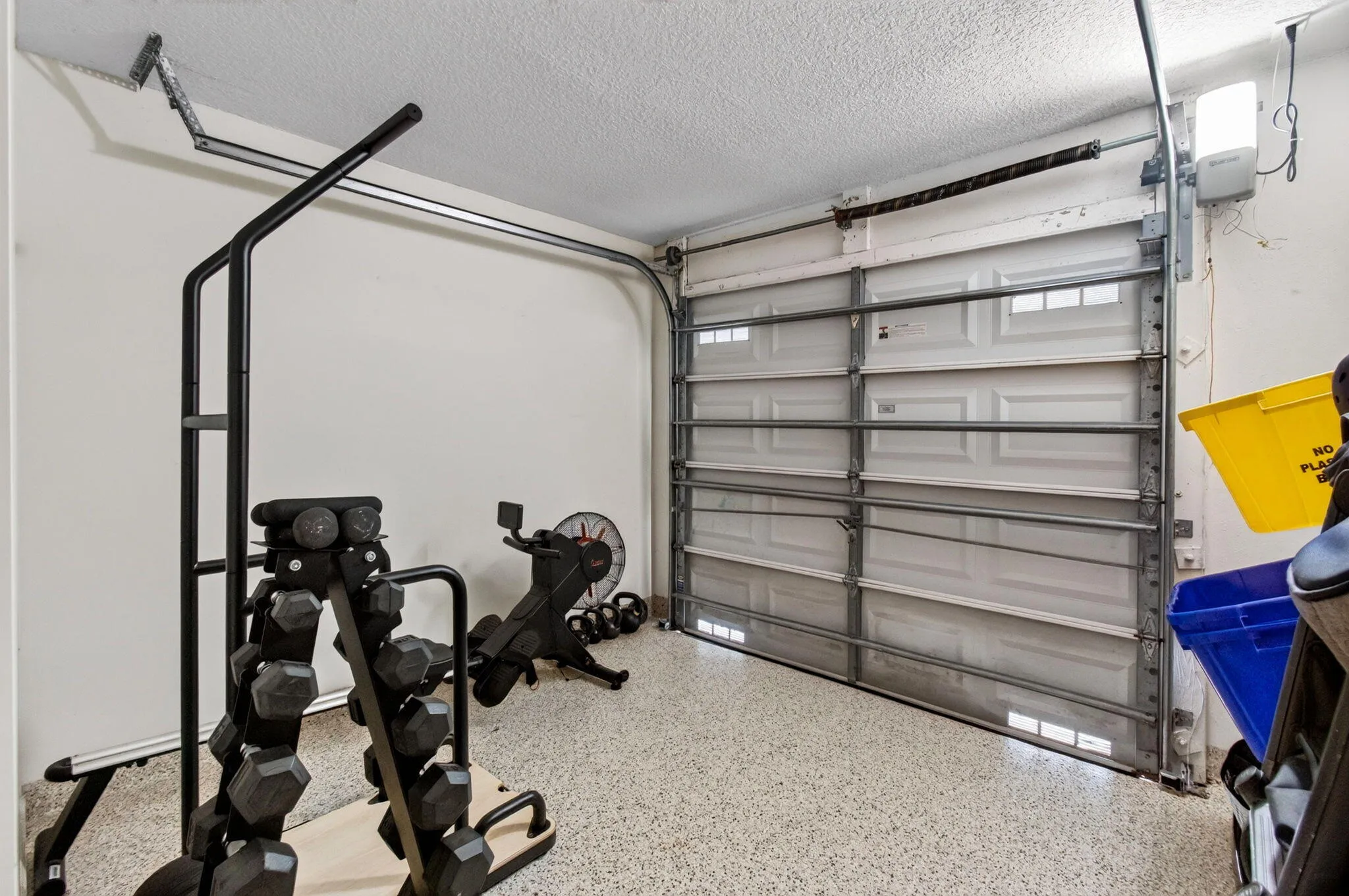 Garage space featuring a paneled overhead door, an automatic garage door opener, and a speckled epoxy floor coating