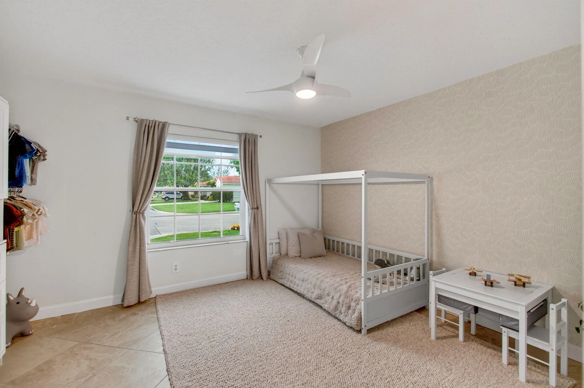 Spacious room featuring a large window with natural light, a modern ceiling fan, a patterned accent wall, and a combination of carpet and tile flooring
