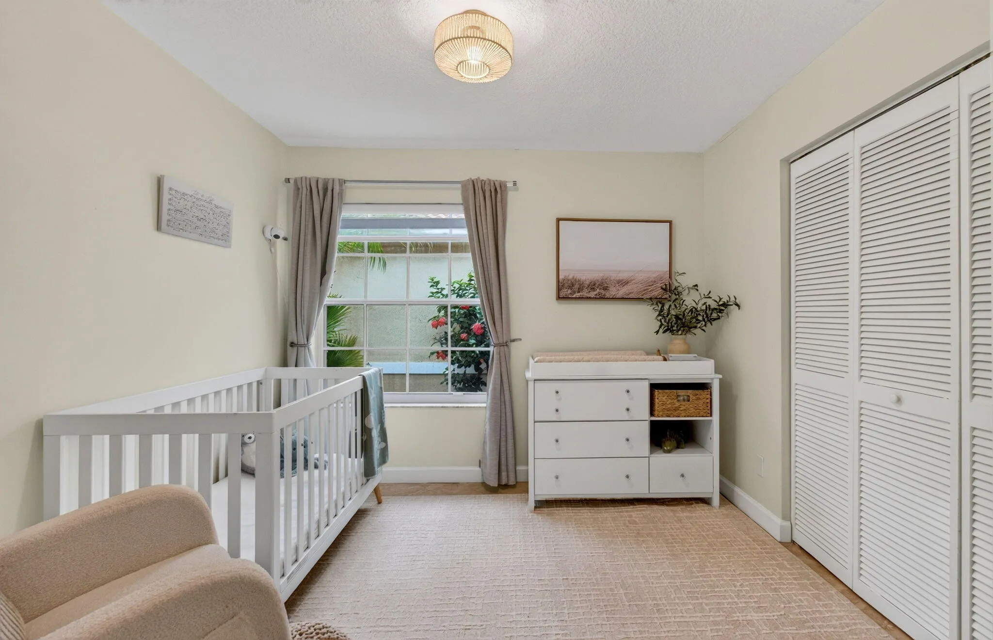 Neutral-toned room featuring a window with exterior foliage, louvered bi-fold closet doors, and light-colored walls