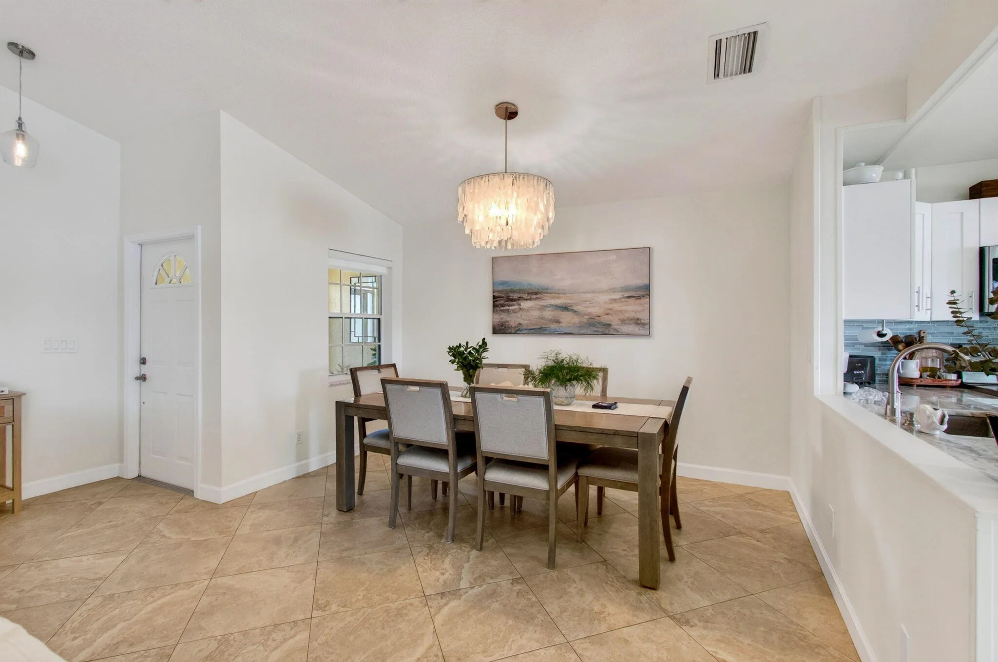 Open-concept dining area featuring a prominent chandelier, vaulted ceiling, and large tile flooring