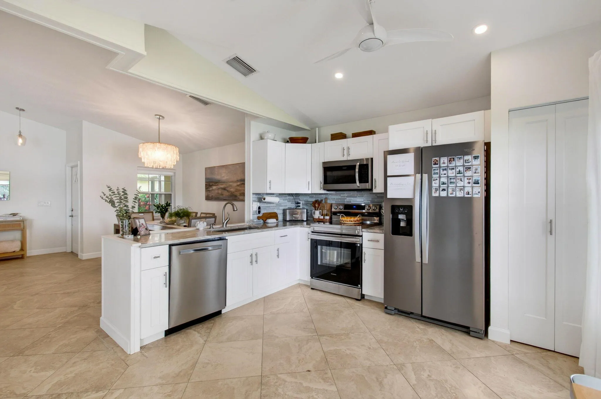 Modern kitchen featuring stainless steel appliances, white cabinetry, a kitchen island with sink, neutral tile flooring, and recessed lighting