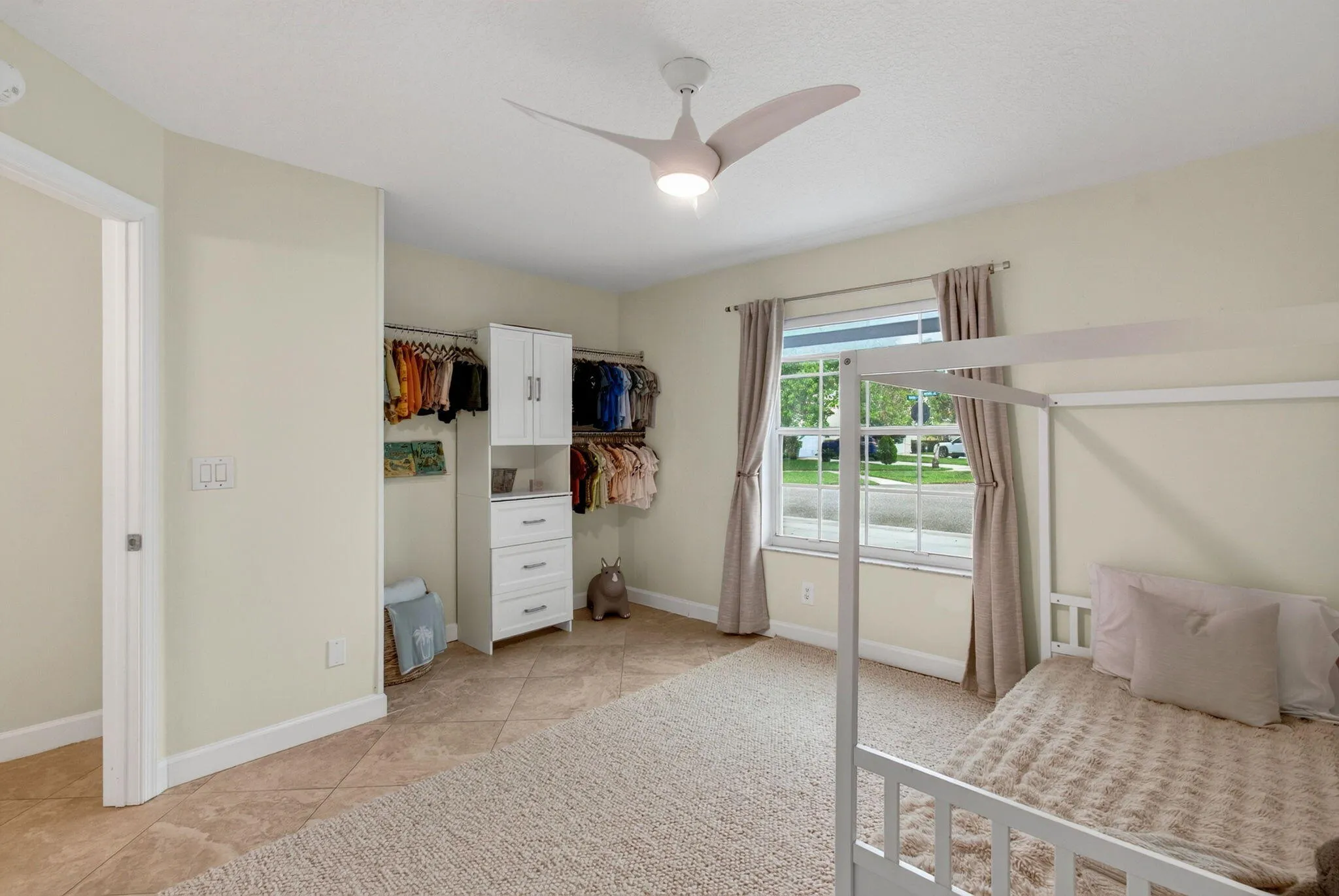 Spacious room featuring a large window, tile flooring, carpet flooring, a modern ceiling fan, and an open closet system with integrated cabinetry and drawers