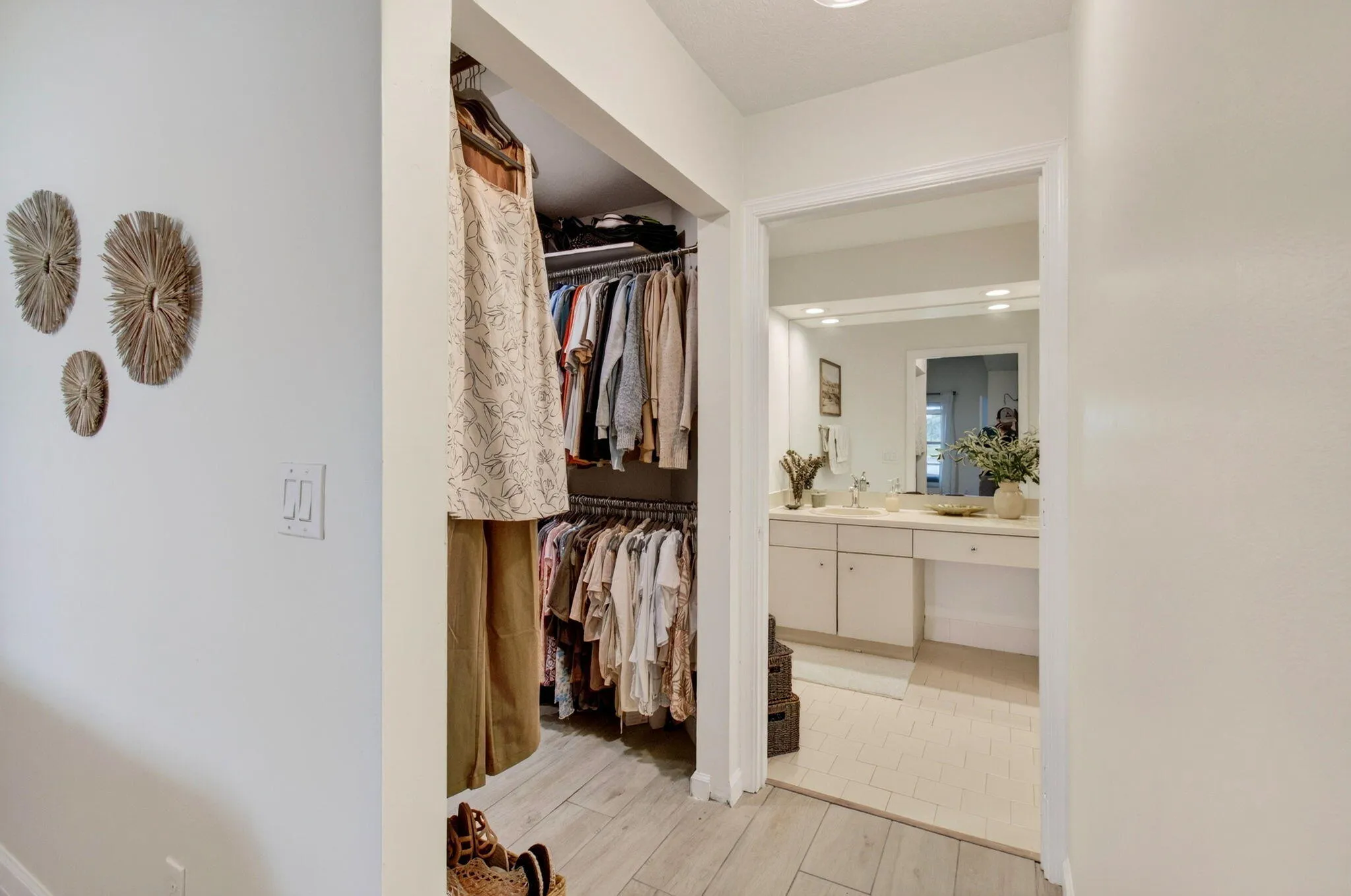 Walk-in closet featuring wood-finish flooring and built-in shelving, opening to a vanity area with an integrated sink, broad mirror, and overhead lighting