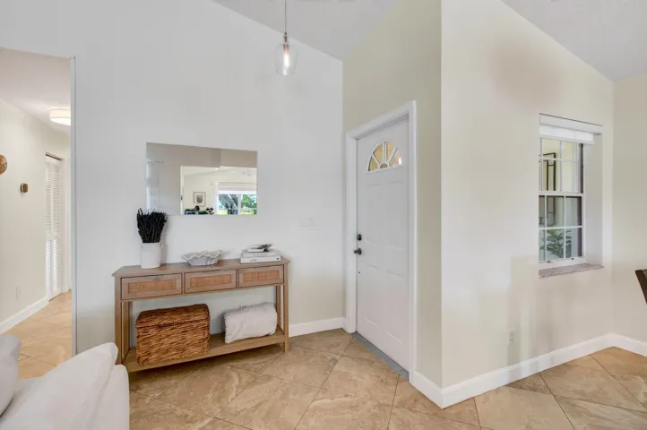 Entryway featuring a vaulted ceiling with a pendant light fixture, ceramic tile flooring, a white paneled door with an arched glass insert.