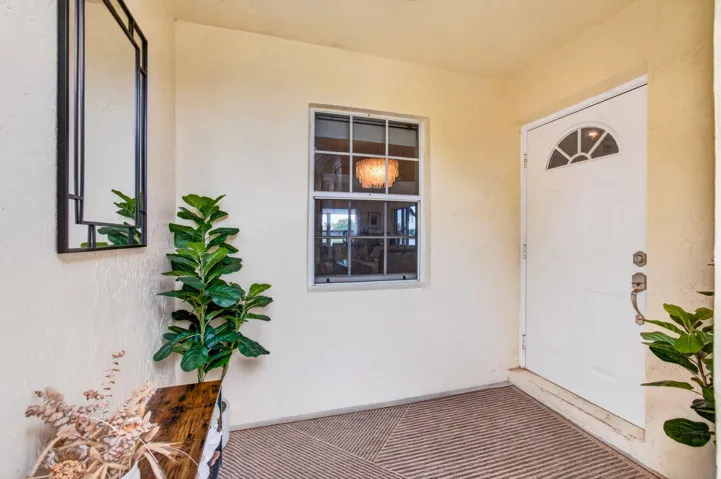 Covered entry with a white paneled door featuring an arched window, textured wall finish, and neutral floor covering