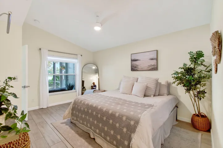 Bright interior space featuring light wood-finish flooring, a window with exterior views, and a vaulted ceiling with a flush-mount ceiling fan
