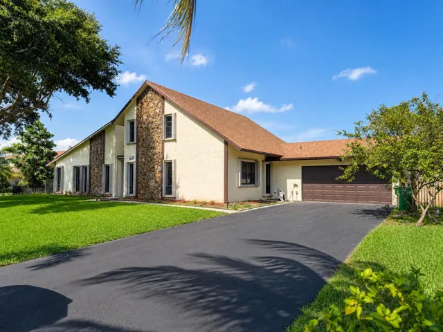 Spacious residence featuring a stucco exterior with stone accents, a brown shingle roof, an attached garage, and a paved driveway