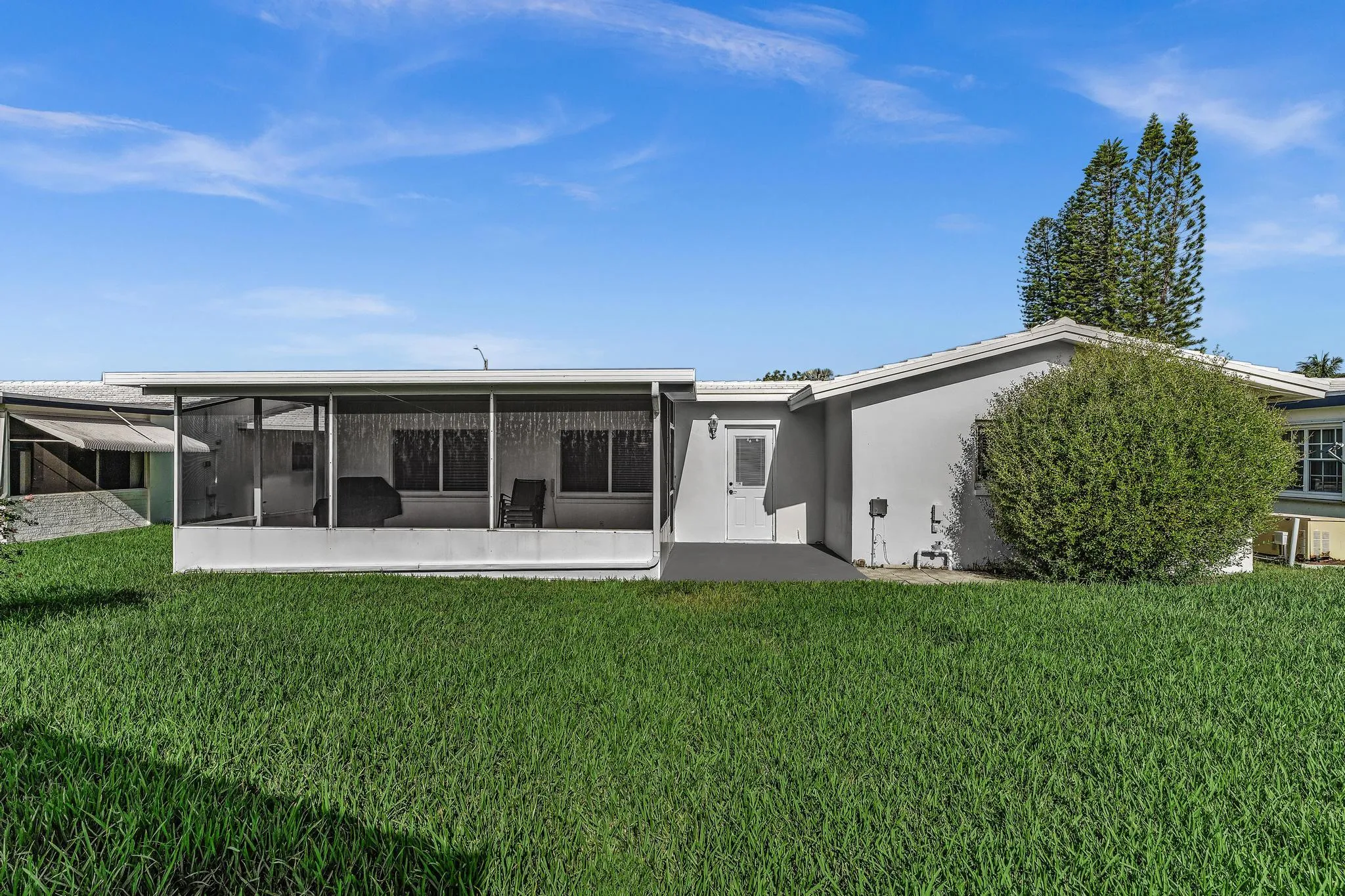 Rear exterior featuring a large screened patio, stucco siding, and a lush green lawn