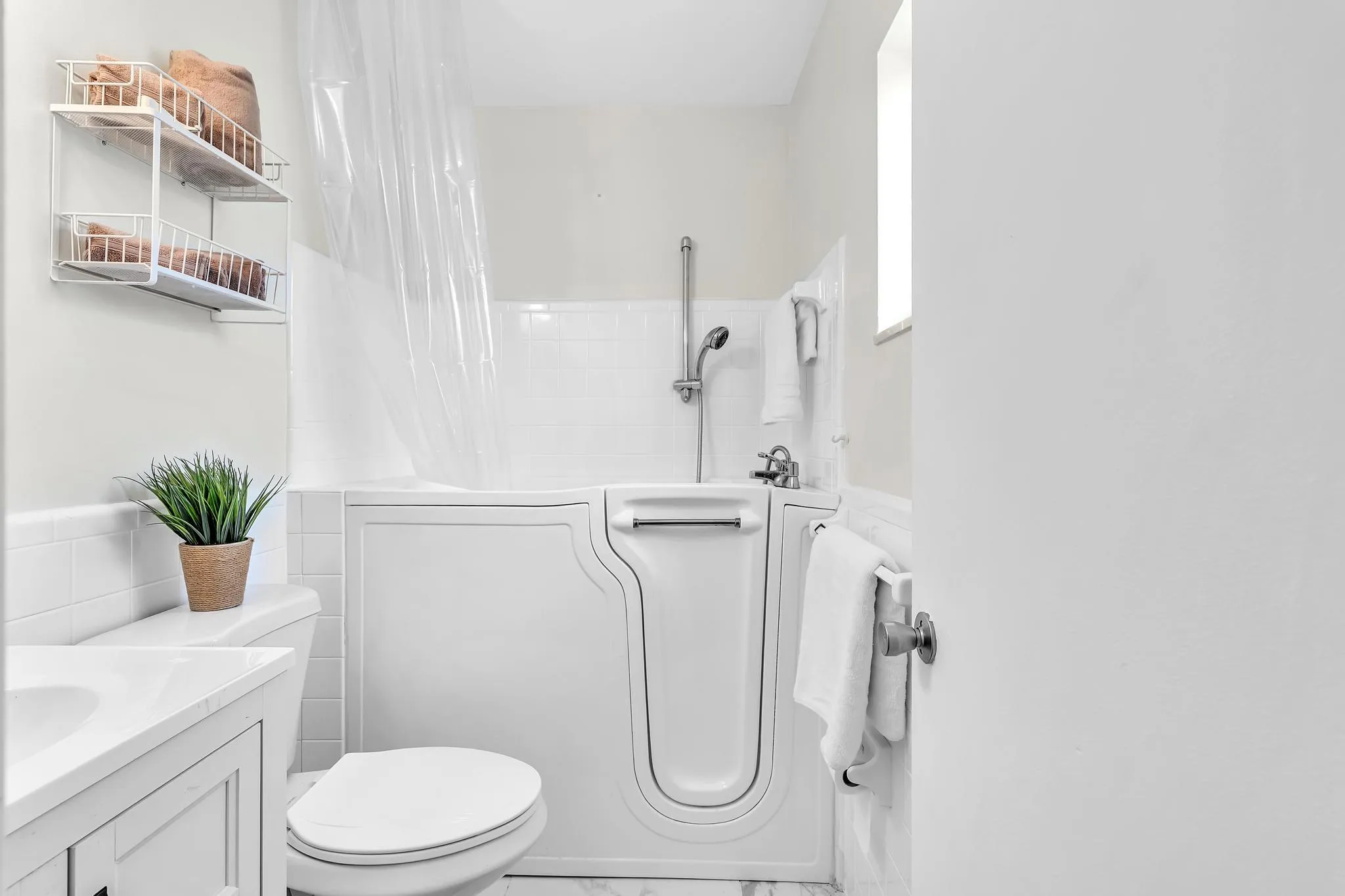 Bathroom featuring a walk-in tub with showerhead, white subway tile surround, tile flooring, and a vanity with an integrated sink