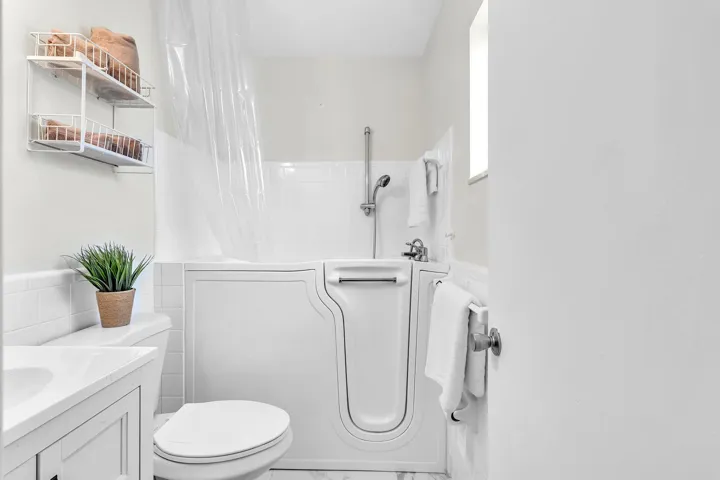 Bathroom featuring a walk-in tub with showerhead, white subway tile surround, tile flooring, and a vanity with an integrated sink