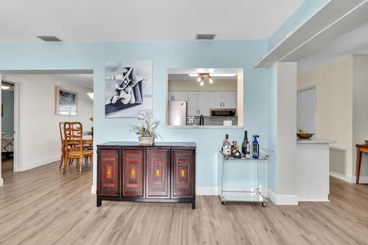 Open-concept living area featuring wood-finish flooring, light blue and cream wall paint, and a pass-through window to the kitchen