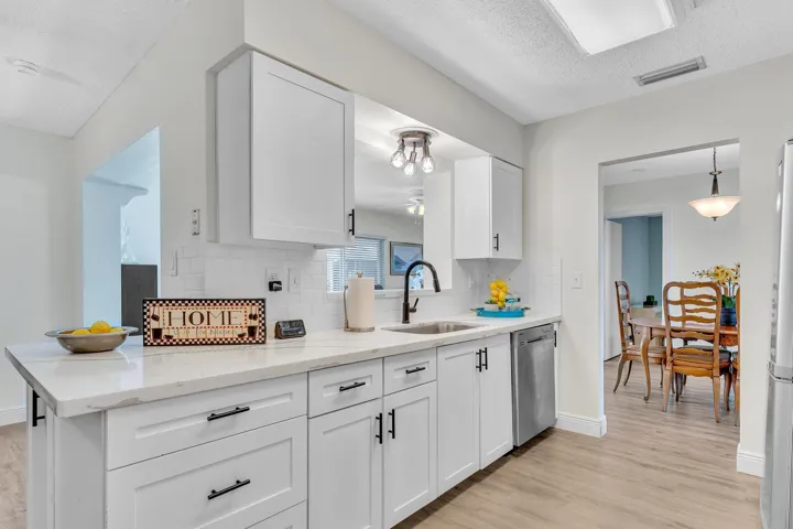 Modern kitchen featuring white shaker-style cabinetry, a light-toned countertop, a subway tile backsplash, stainless steel appliances, and wood-finish flooring