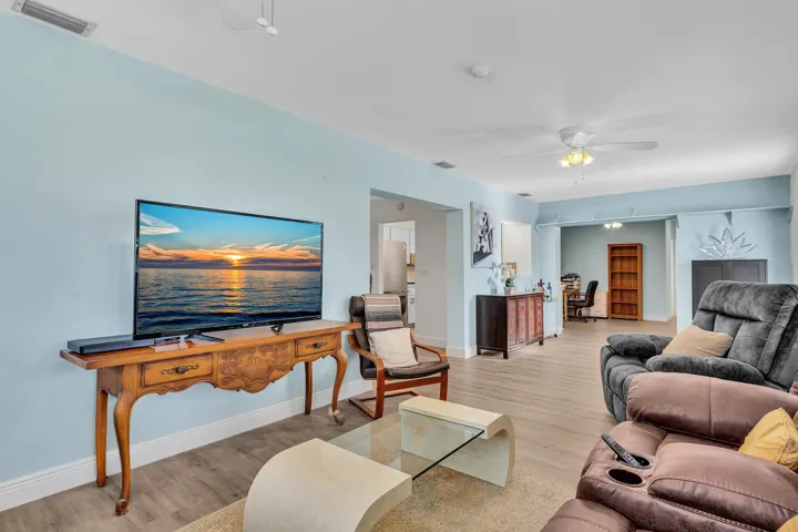 Spacious living area featuring light wood-finish flooring, a ceiling fan, and light blue walls