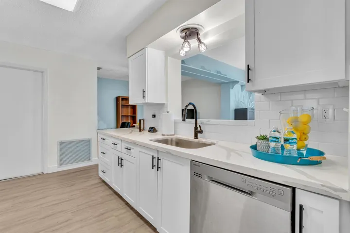 Kitchen featuring white shaker-style cabinetry, stainless steel dishwasher, undermount sink with a matte black faucet, white subway tile backsplash, and light wood-finish flooring