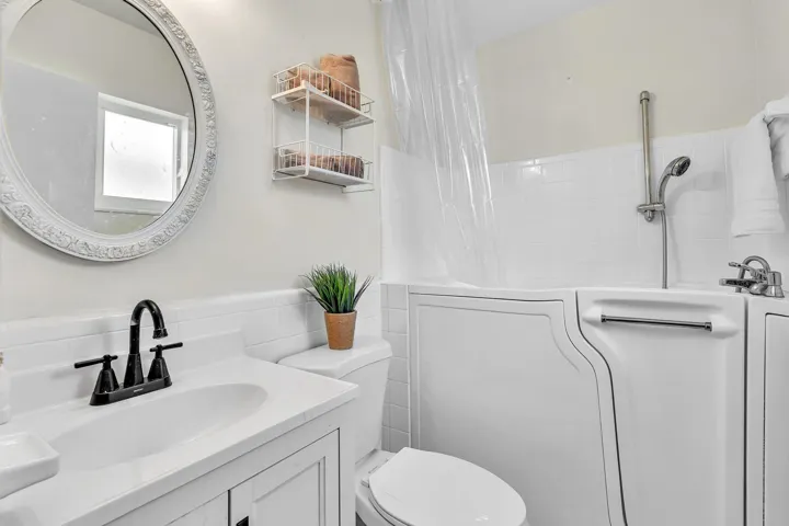 Bathroom featuring a walk-in tub with a hand shower, white subway tile surround, and a white vanity with a dark bronze faucet