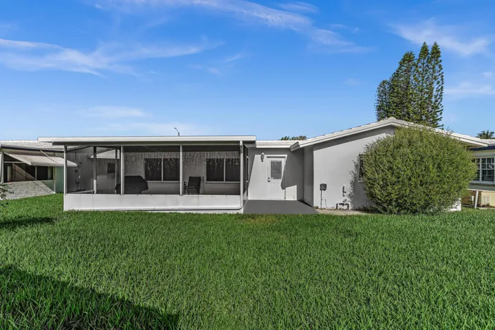 Rear exterior featuring a large screened patio, stucco siding, and a lush green lawn