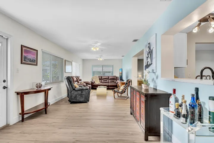 Open-concept living area featuring wood-finish flooring, multiple windows with horizontal blinds, and ceiling fans