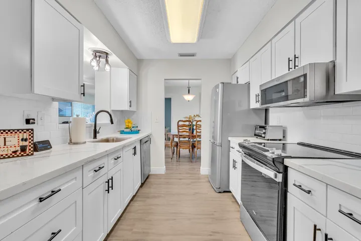 Galley kitchen featuring white cabinetry, light-colored countertops, stainless steel appliances, and wood-finish flooring
