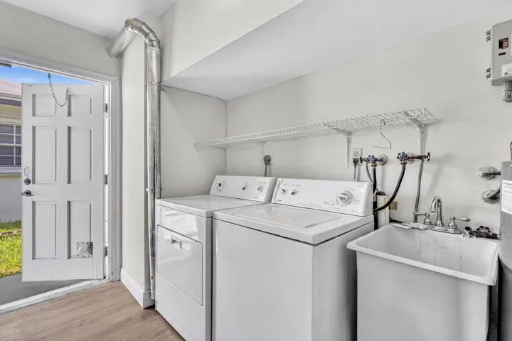 Dedicated laundry area featuring a utility sink, overhead wire shelving, and wood-finish flooring