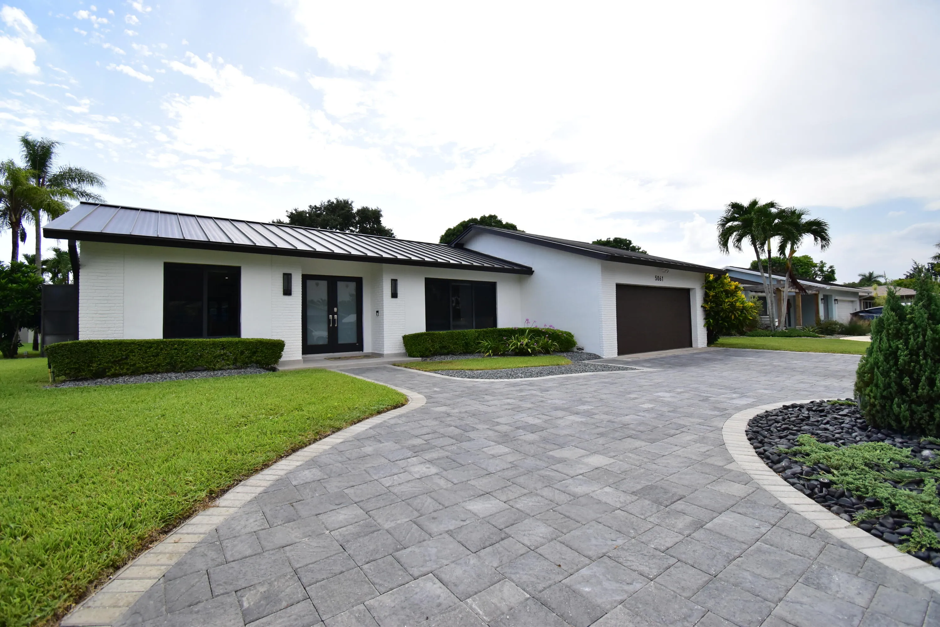 Contemporary residence featuring a black metal roof, white exterior siding, and a paver driveway