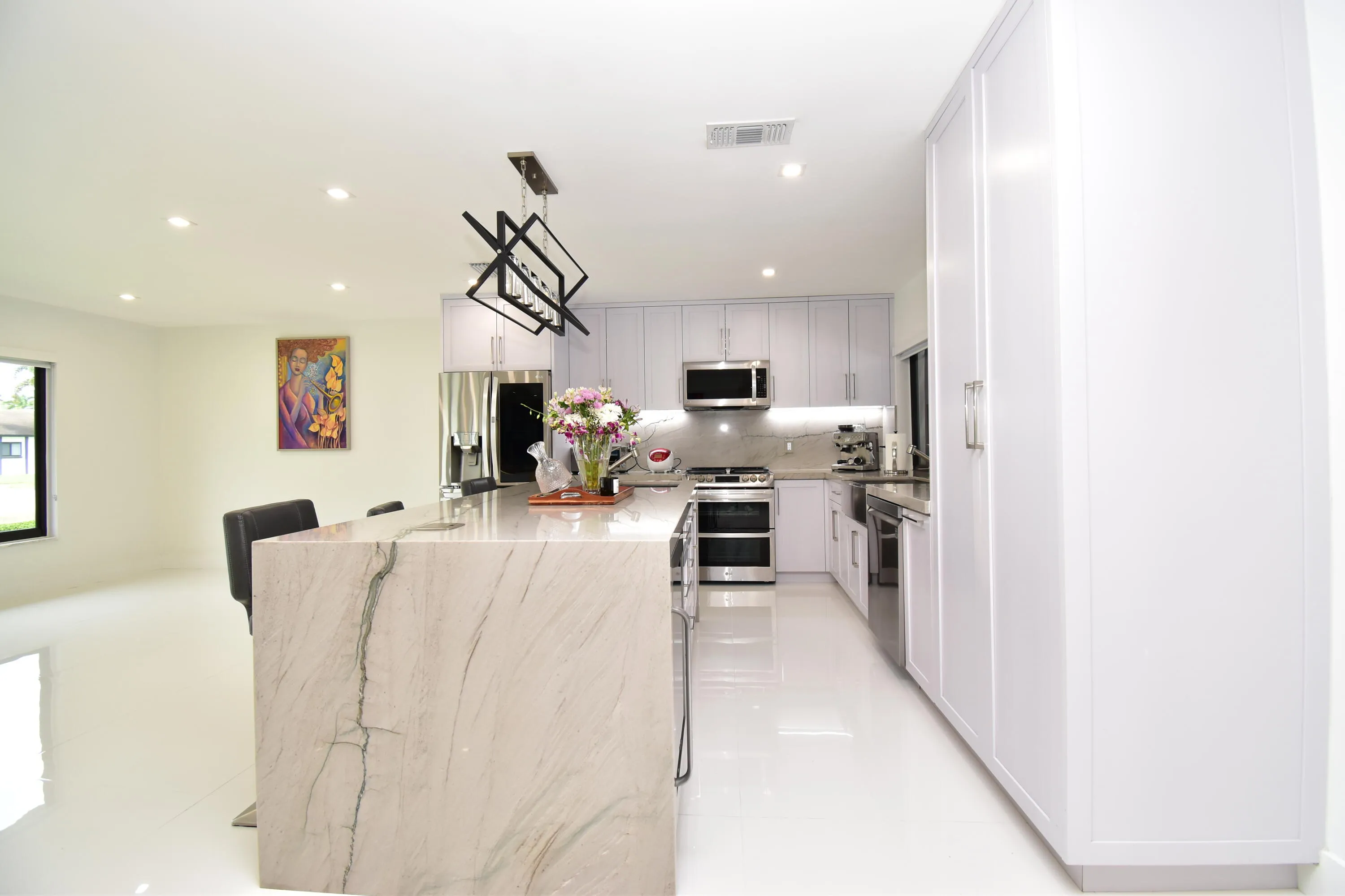 Modern kitchen featuring a waterfall island, stainless steel appliances, white cabinetry, recessed lighting, and a linear chandelier