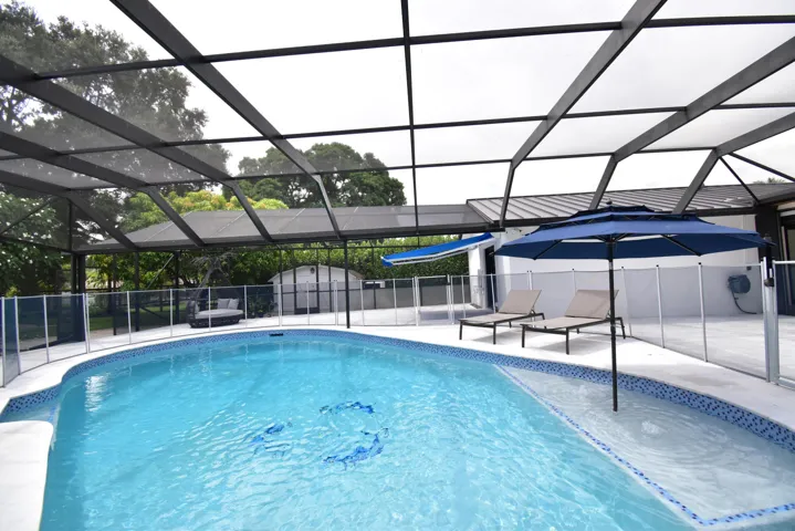Screened-in pool area featuring a curved swimming pool with decorative tile accents and an integrated spa