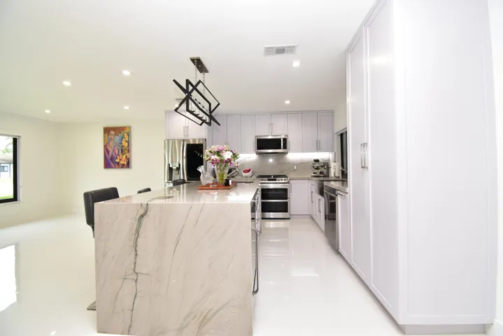 Modern kitchen featuring a waterfall island, stainless steel appliances, white cabinetry, recessed lighting, and a linear chandelier