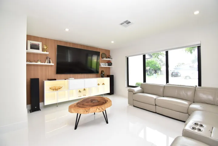 Living space featuring white polished flooring, a large multi-pane window, recessed lighting, and a wood-finish accent wall with floating shelves