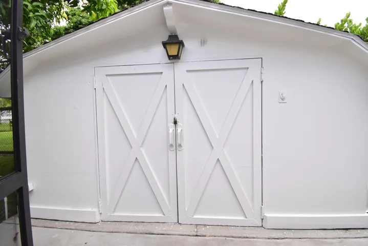 White utility structure featuring barn-style doors with decorative X-bracing