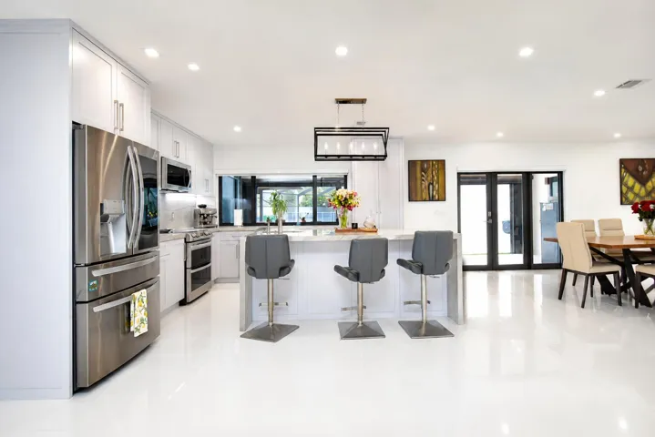 Expansive kitchen featuring white cabinetry, stainless steel appliances, a center island with pendant lighting, and polished white flooring
