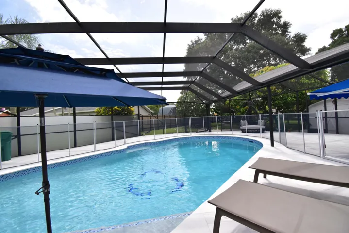 Screened enclosure featuring a freeform swimming pool with blue tile accents, a surrounding pool deck, and a perimeter safety fence