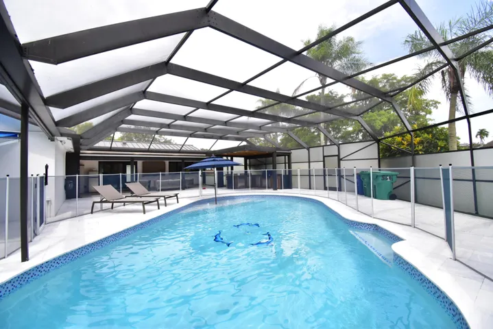 Screened pool enclosure featuring an irregular shaped pool with blue mosaic tile trim, light-colored paver decking, and a removable perimeter fence