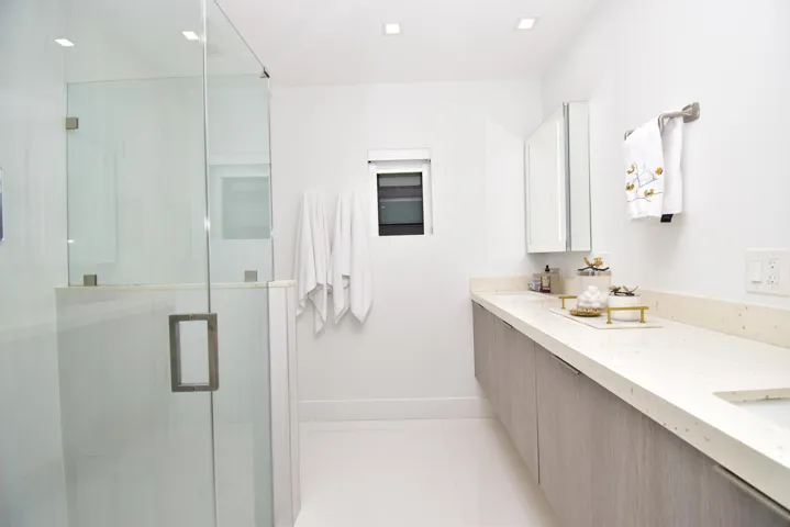 Modern bathroom featuring a frameless glass shower enclosure, a floating vanity with wood-finish cabinetry, a light-toned countertop, and recessed ceiling lighting