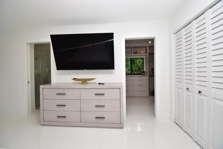 White flooring throughout, featuring a wall-mounted television above a six-drawer dresser with dark hardware