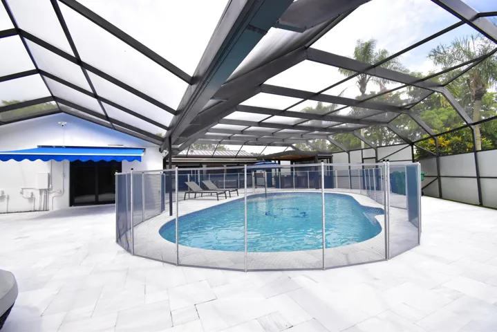 Screen-enclosed pool area featuring a freeform swimming pool with a surrounding safety fence
