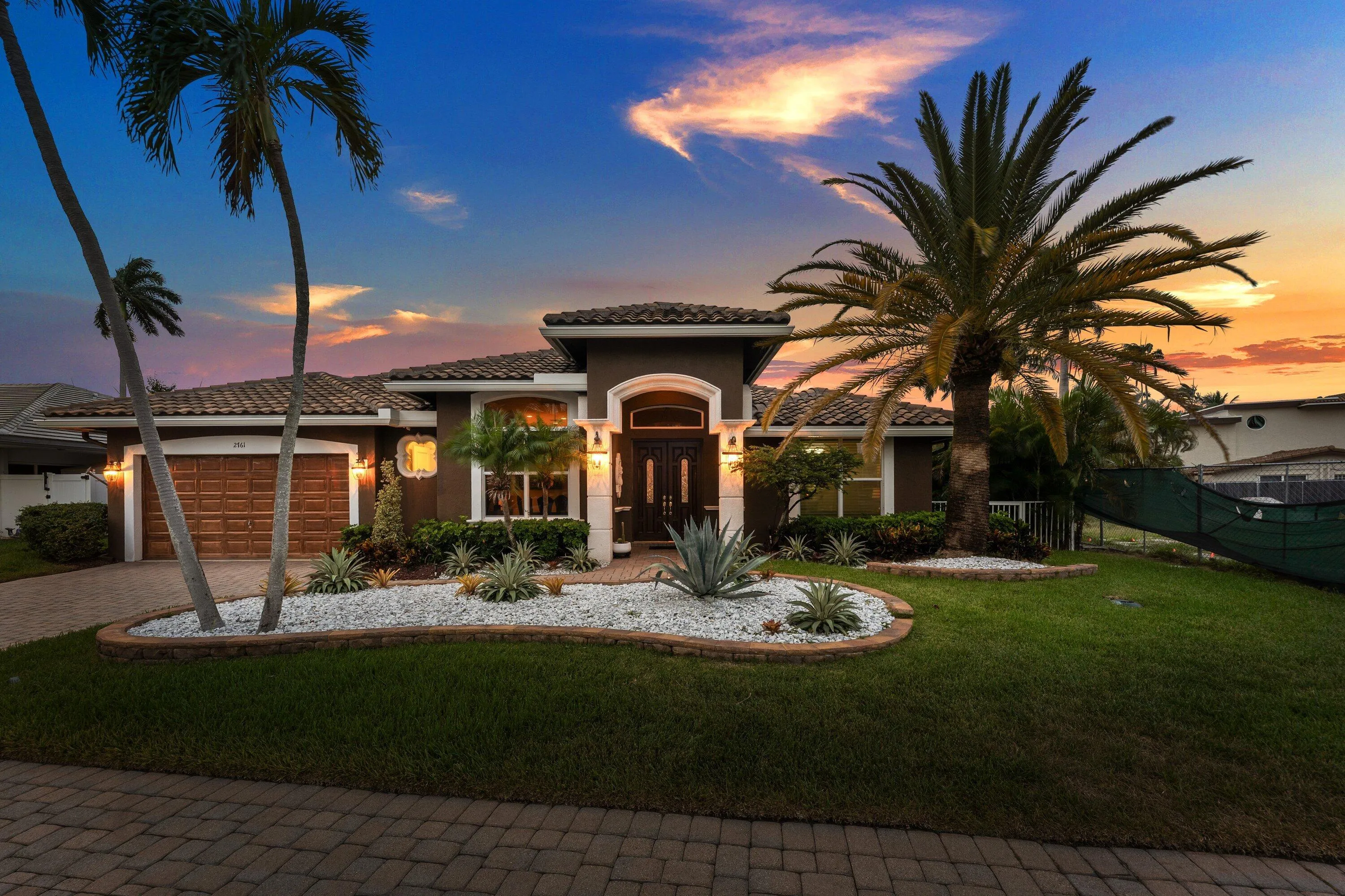 Mediterranean-style residence featuring a tile roof, decorative white stone landscaping, and mature palm trees