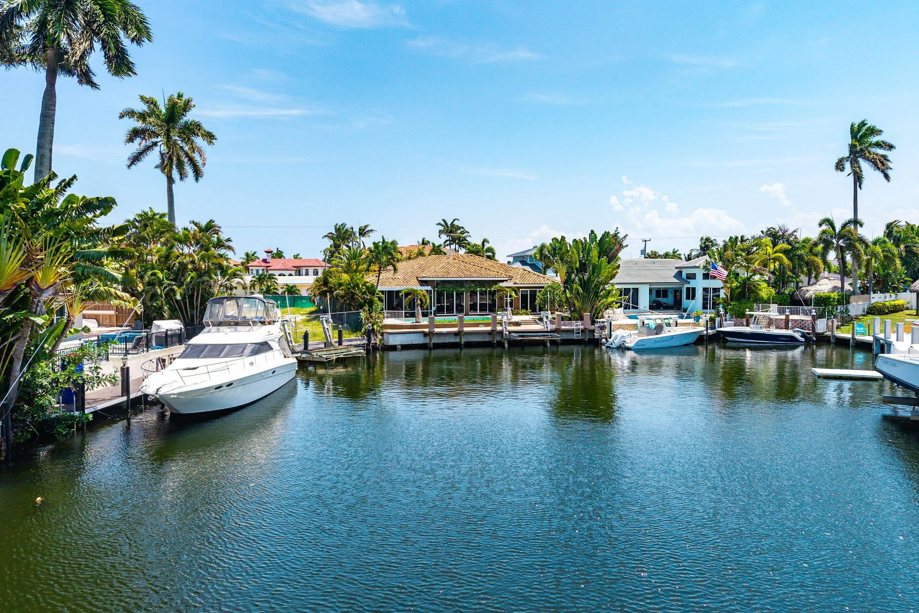 Waterfront property featuring a private boat dock, mature palm trees, and lush tropical landscaping