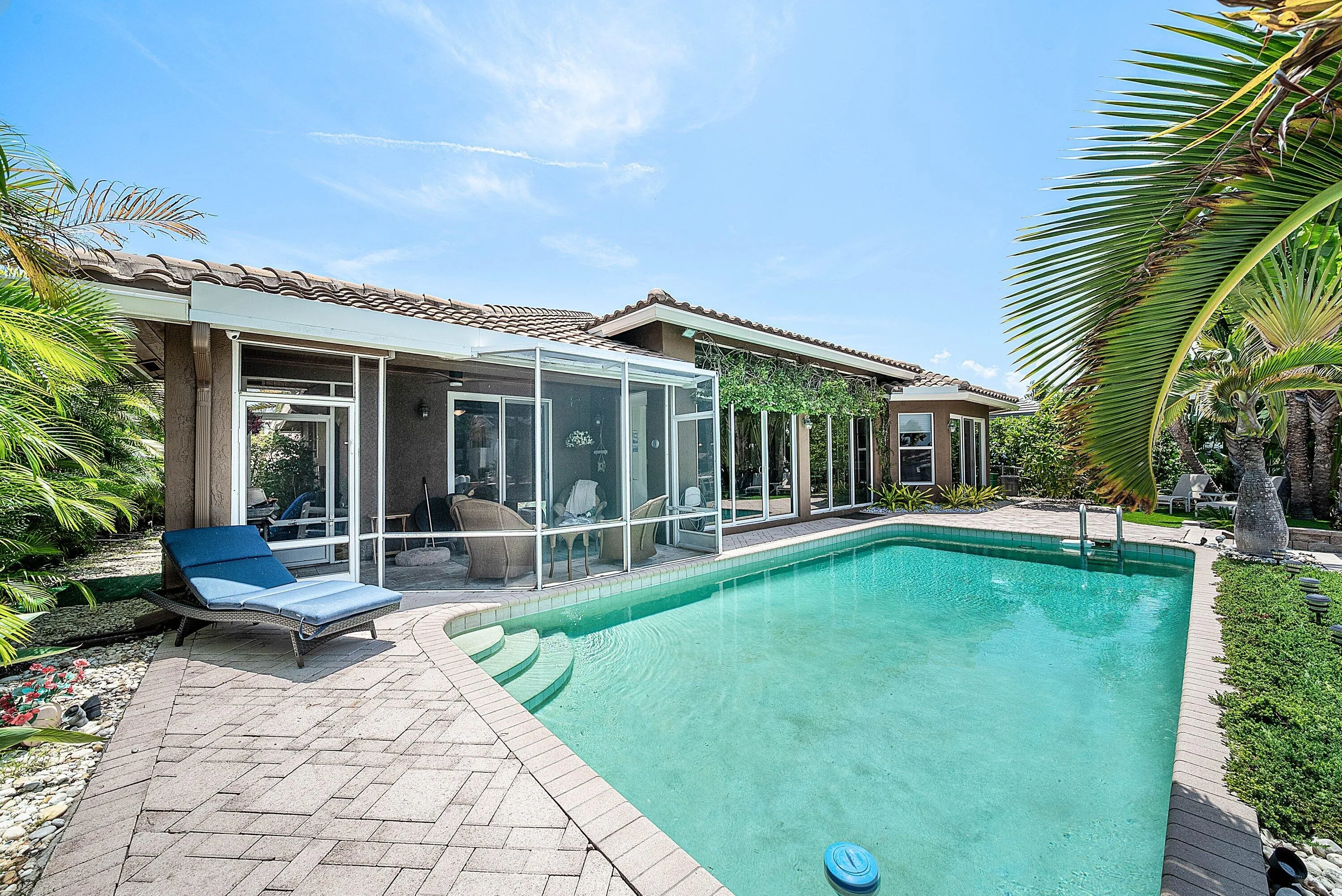 Outdoor swimming pool with integrated steps, surrounded by a paved patio and lush landscaping