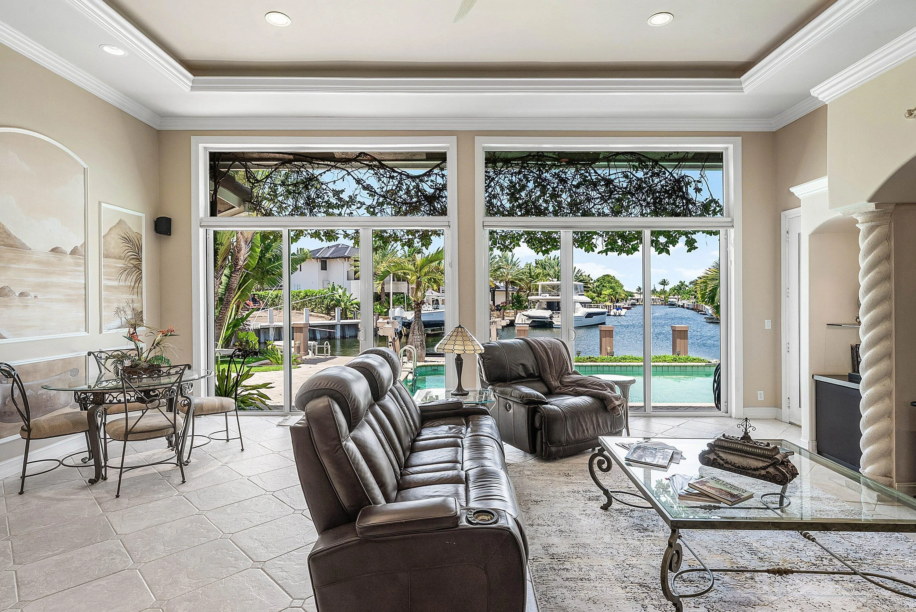 Living area featuring extensive window walls, recessed lighting, tray ceiling, tile flooring, and direct water frontage with a pool