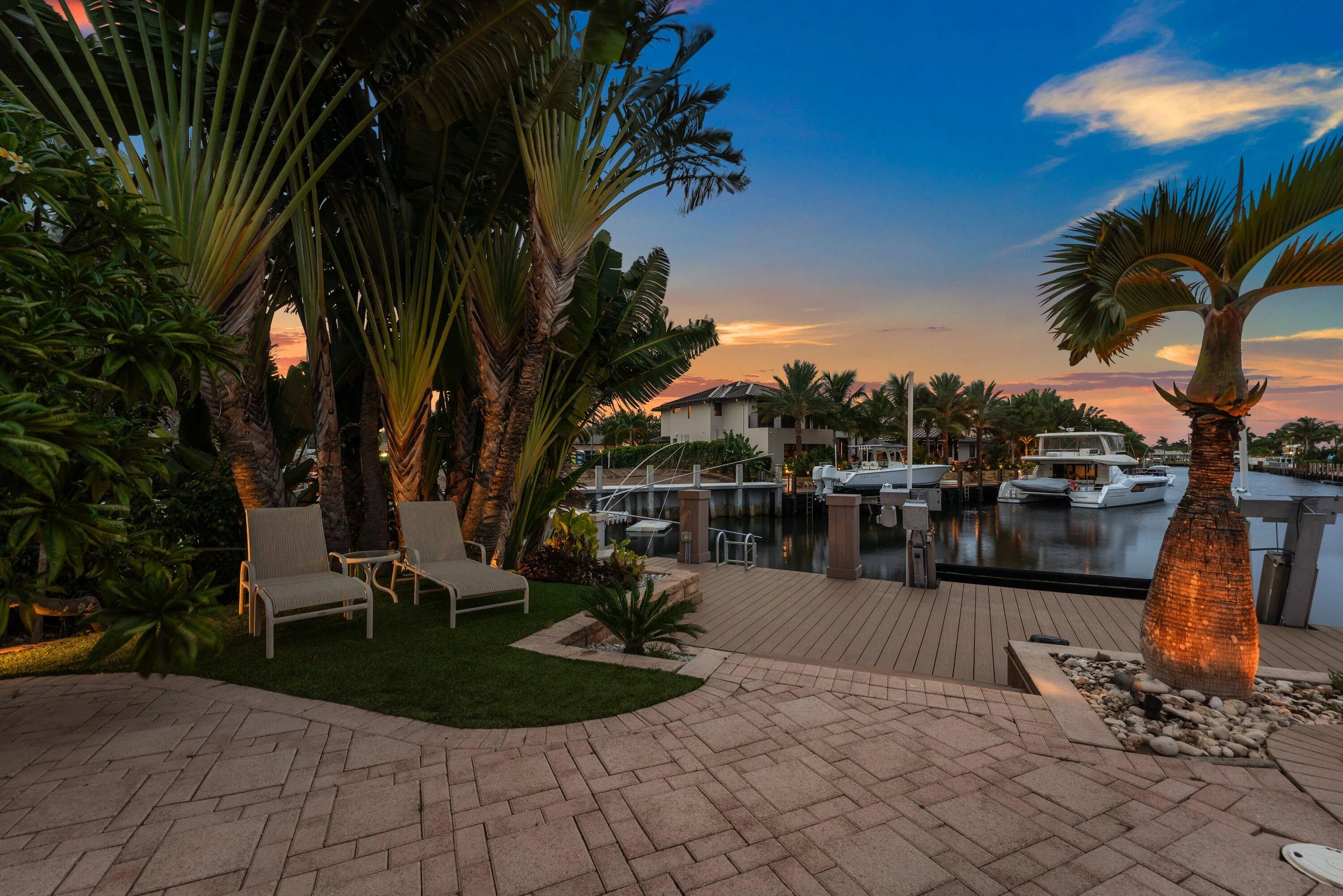 Waterside patio featuring paver stones, a wooden dock, and mature tropical landscaping