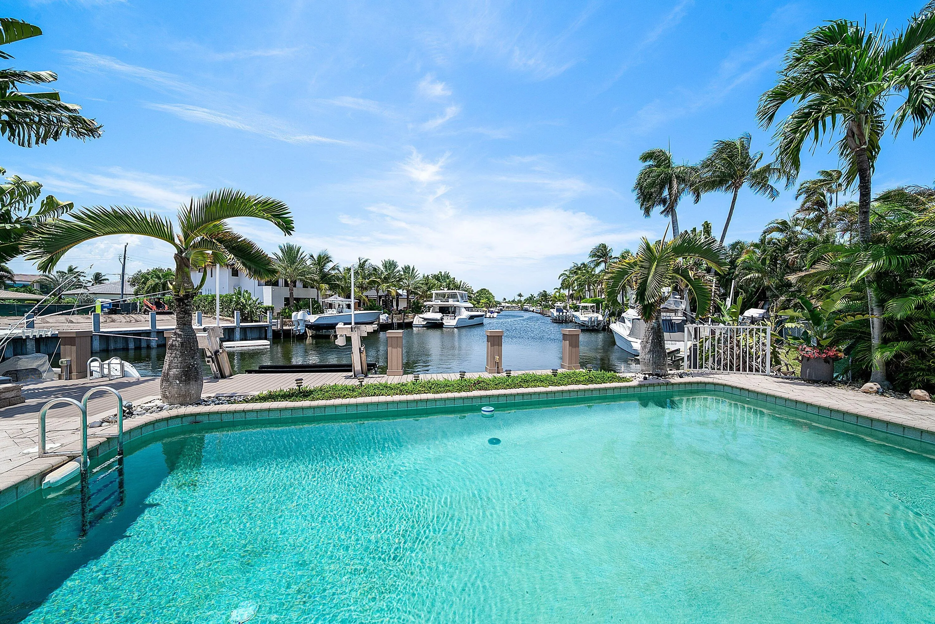 Outdoor swimming pool with integrated steps, surrounded by a paved patio and lush tropical landscaping