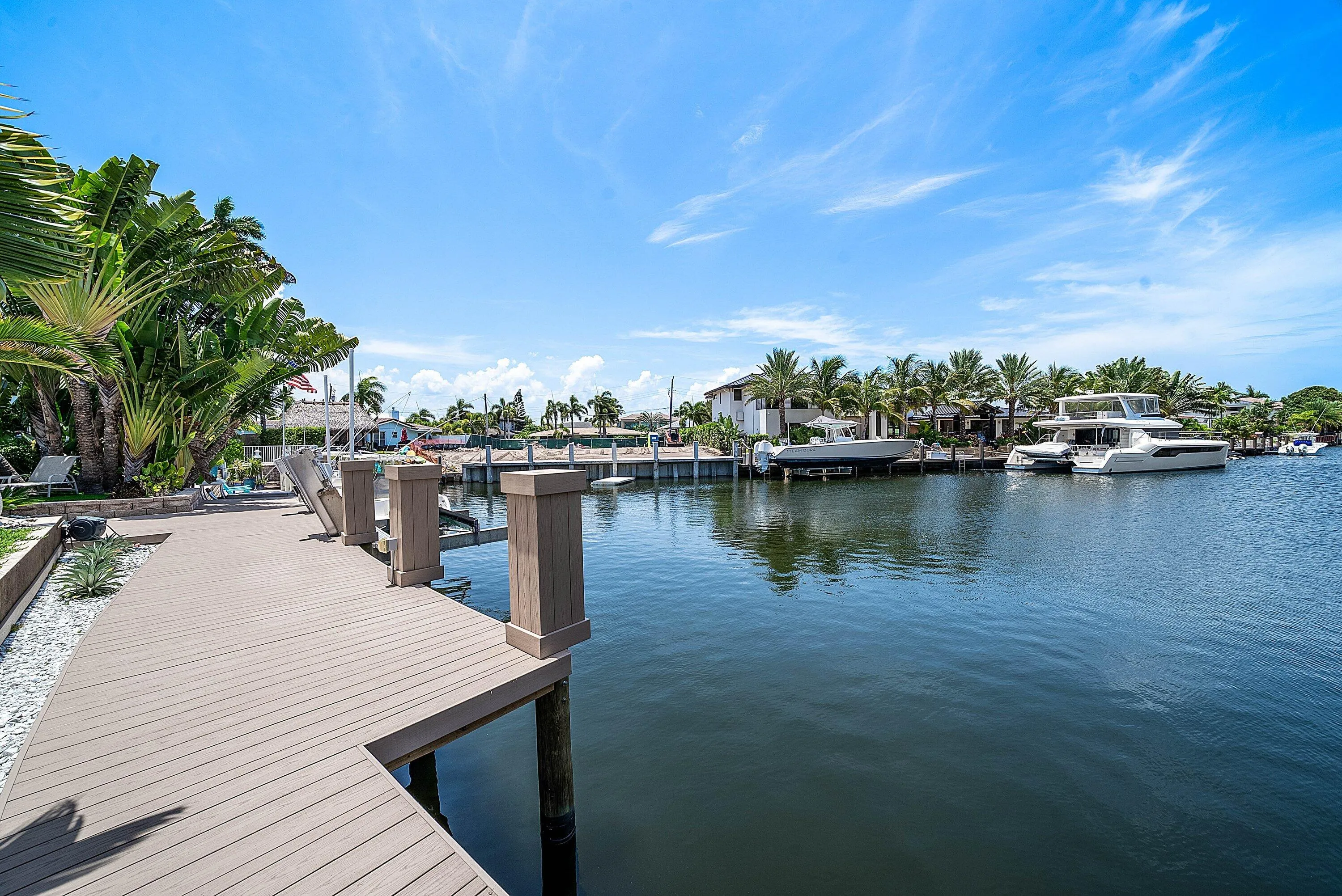 Waterfront property featuring a composite dock, boat lift, and mature tropical landscaping