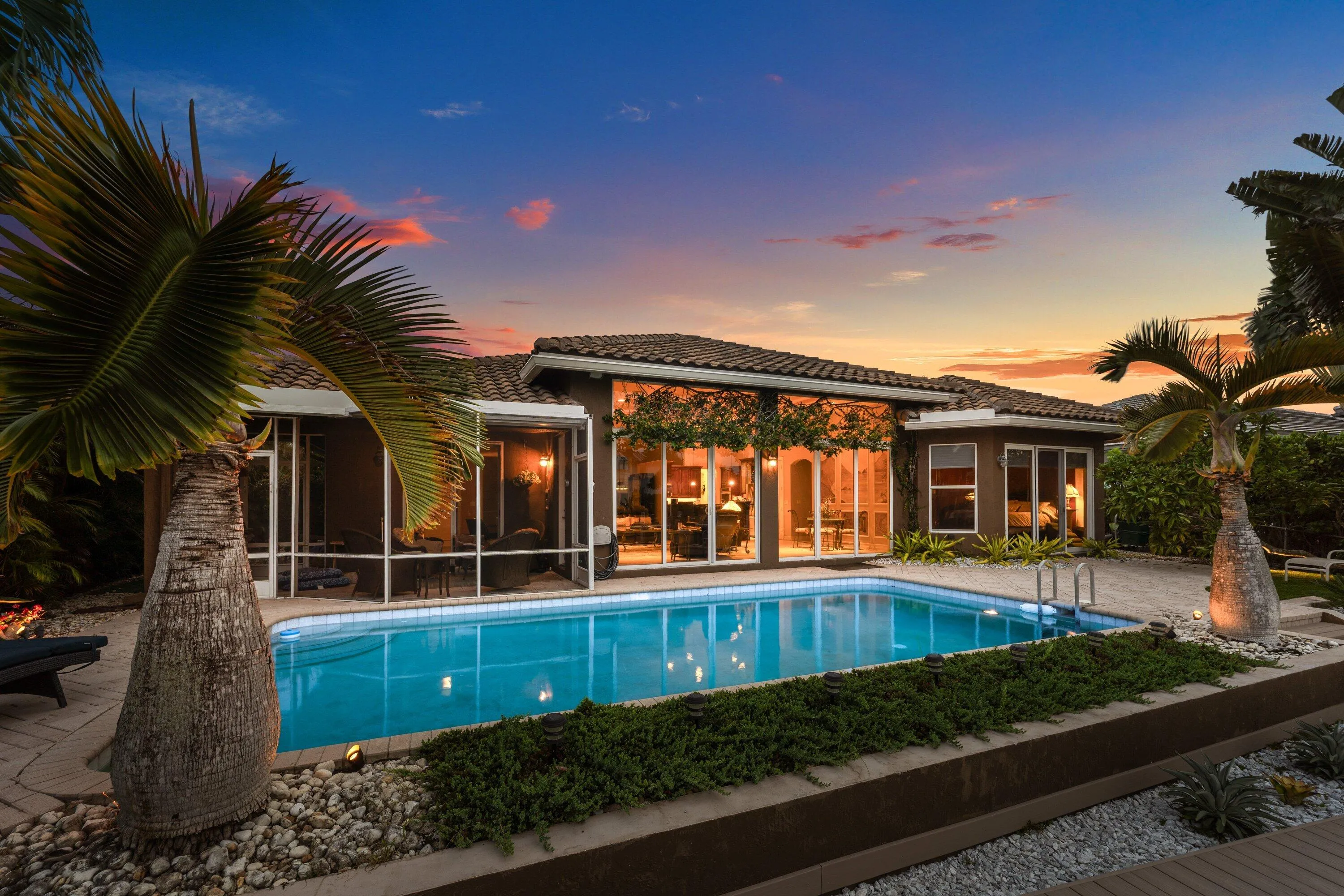 Backyard oasis featuring a swimming pool with integrated steps, surrounded by paver decking and mature palm trees