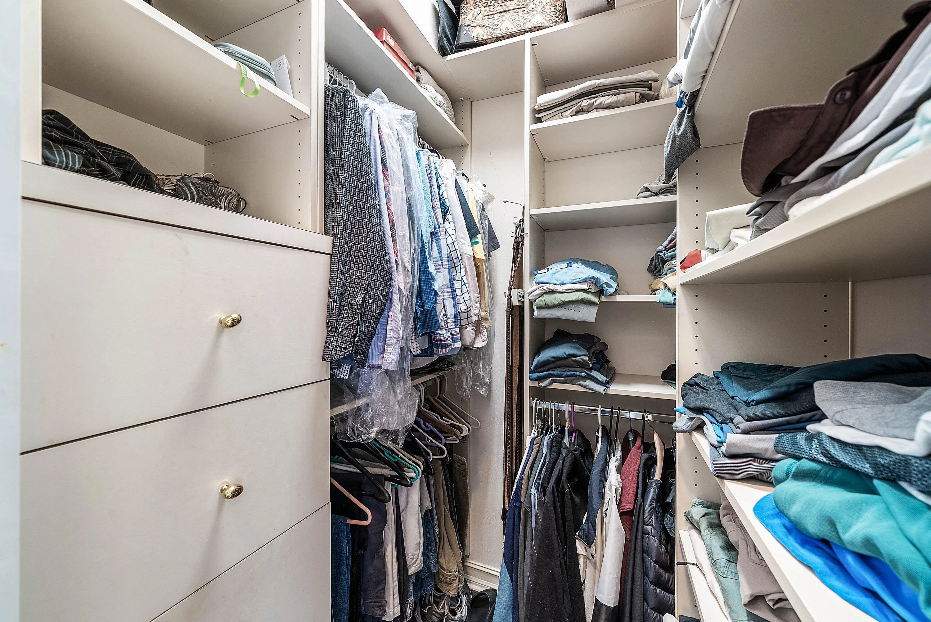 Built-in closet system featuring white shelving and drawer units with gold-tone hardware, providing extensive storage options