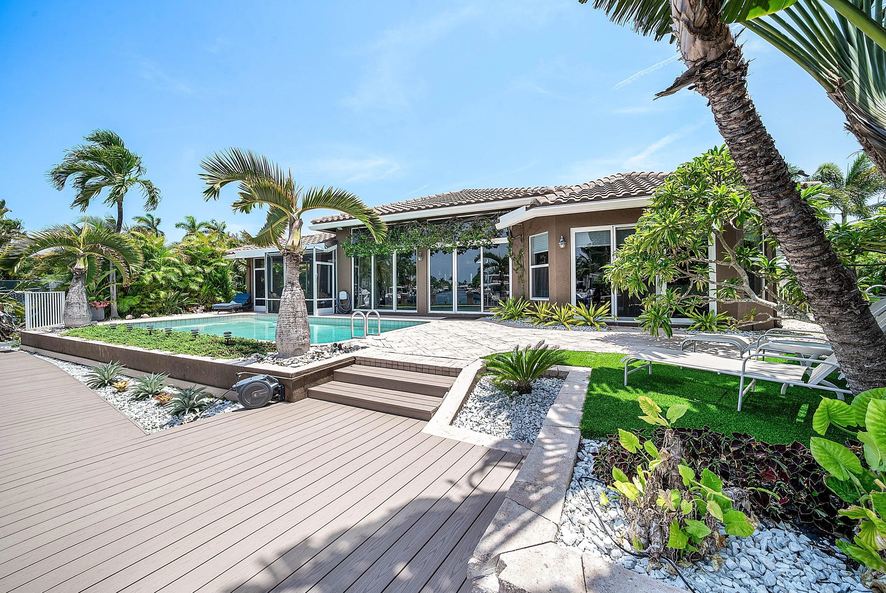 Expansive outdoor living area featuring a swimming pool, composite decking, and mature tropical landscaping